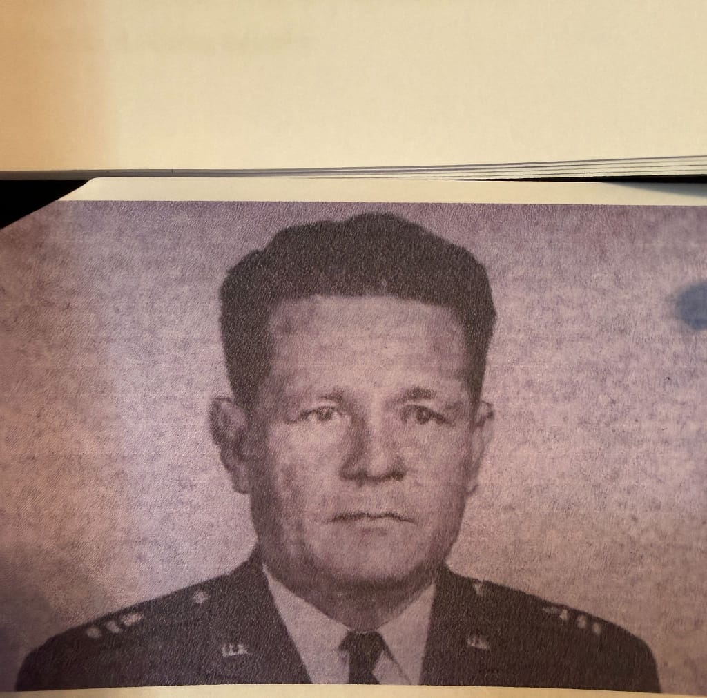 A black and white portrait of a man in a military uniform, with a serious expression. He has short hair and is wearing insignia on his shoulders.