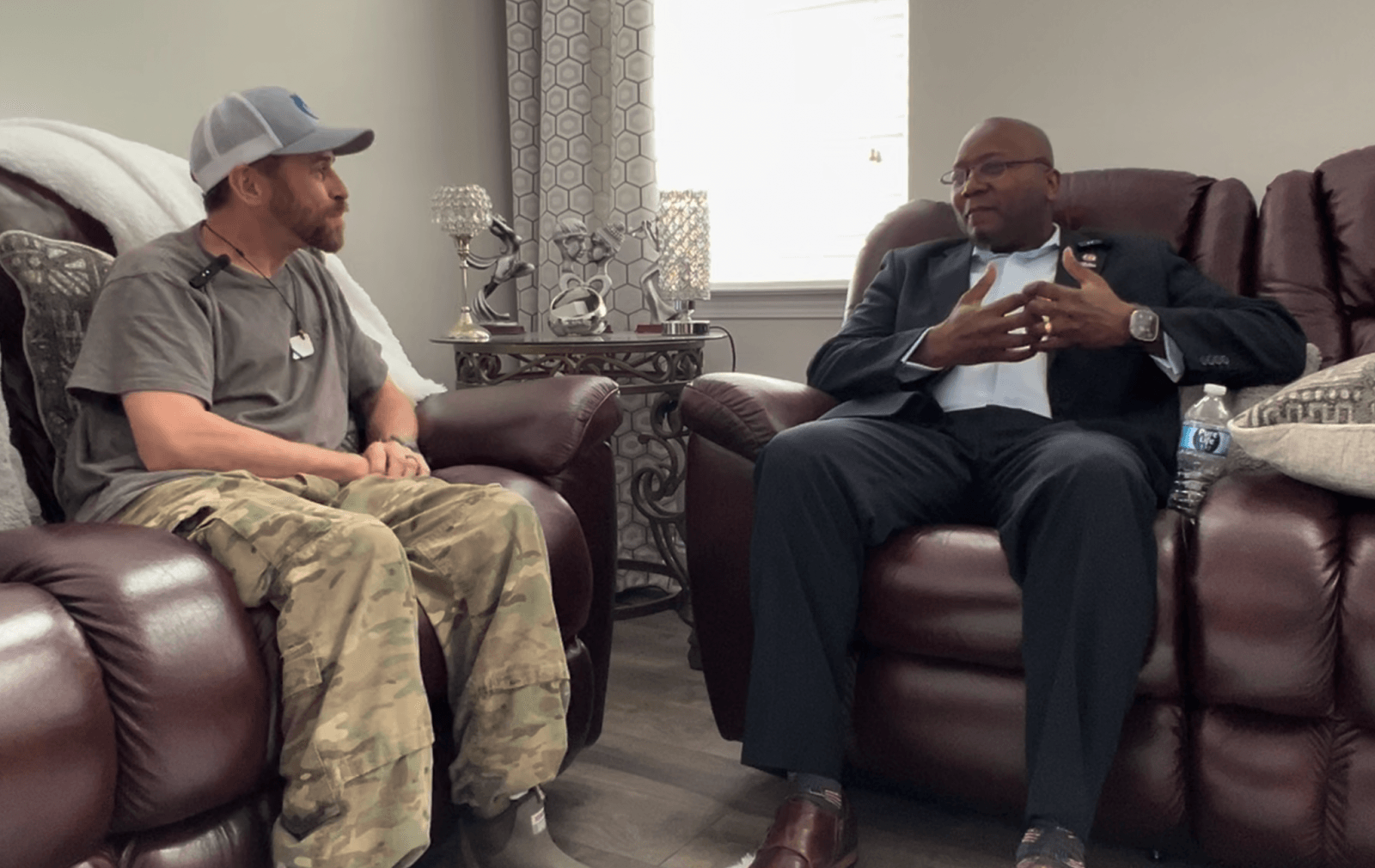 Two men sitting in plush chairs engaged in conversation in a cozy living room.