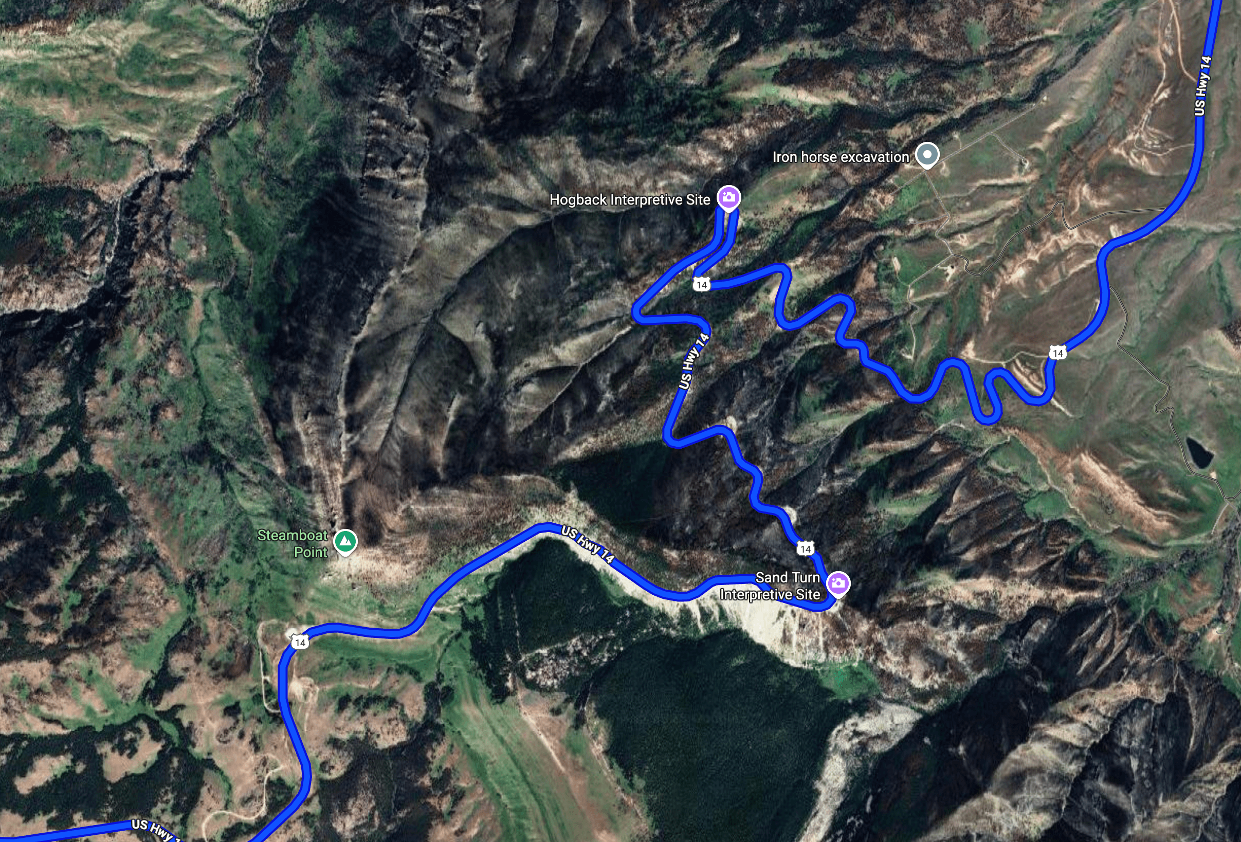 Aerial view of a winding road through mountainous terrain in the Bighorn National Forest, showcasing sharp curves and steep grades.