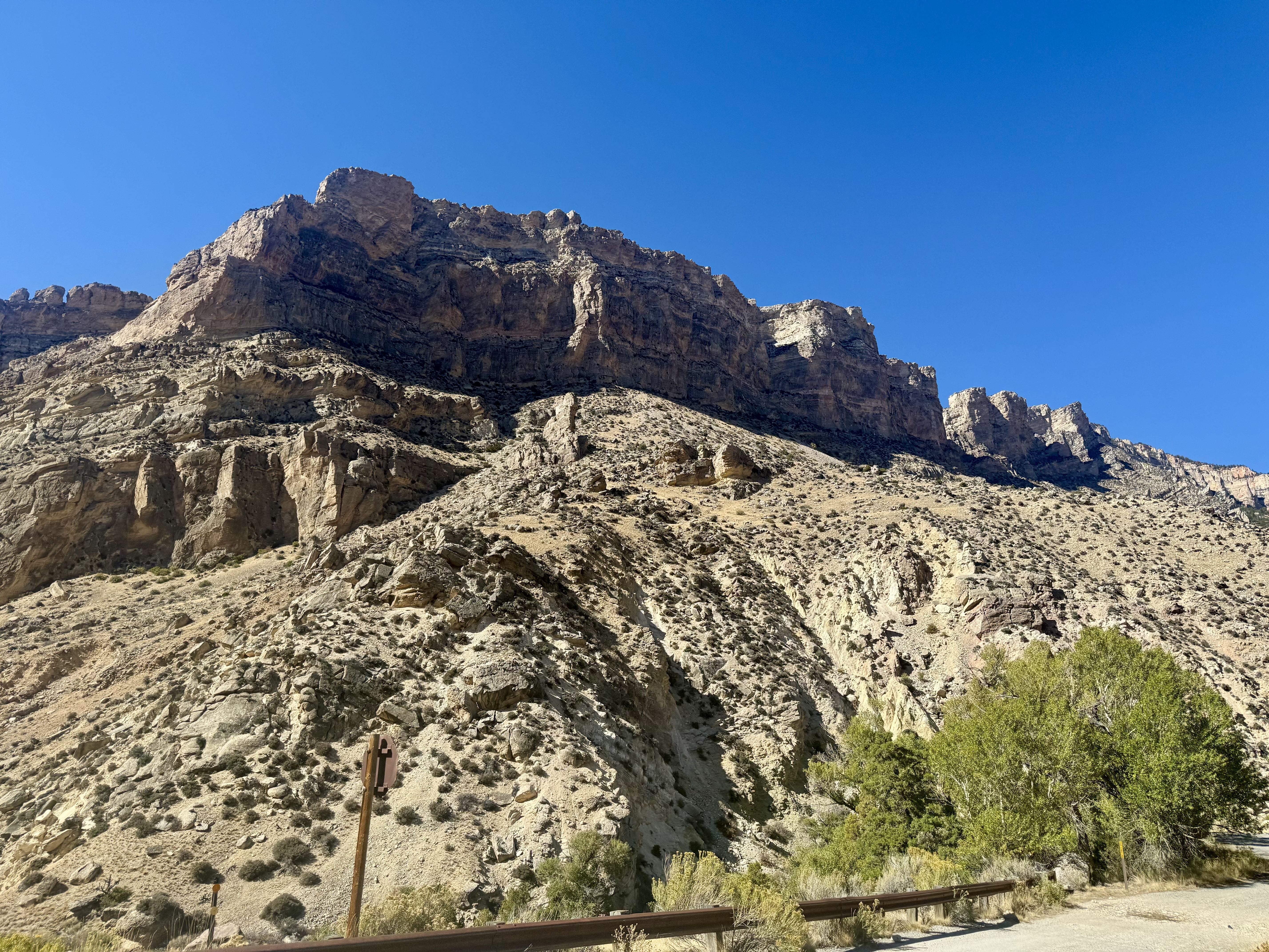 A steep mountain landscape in the Bighorn National Forest under a clear blue sky, featuring rugged rock formations and sparse vegetation.