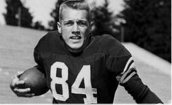 Black and white image of a young male football player wearing jersey number 84, running with a football in hand, set against a stadium backdrop.