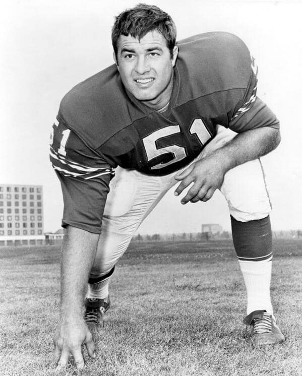 A vintage black-and-white photograph of a football player in a jersey with the number 51, crouching in a stance on a grassy field.