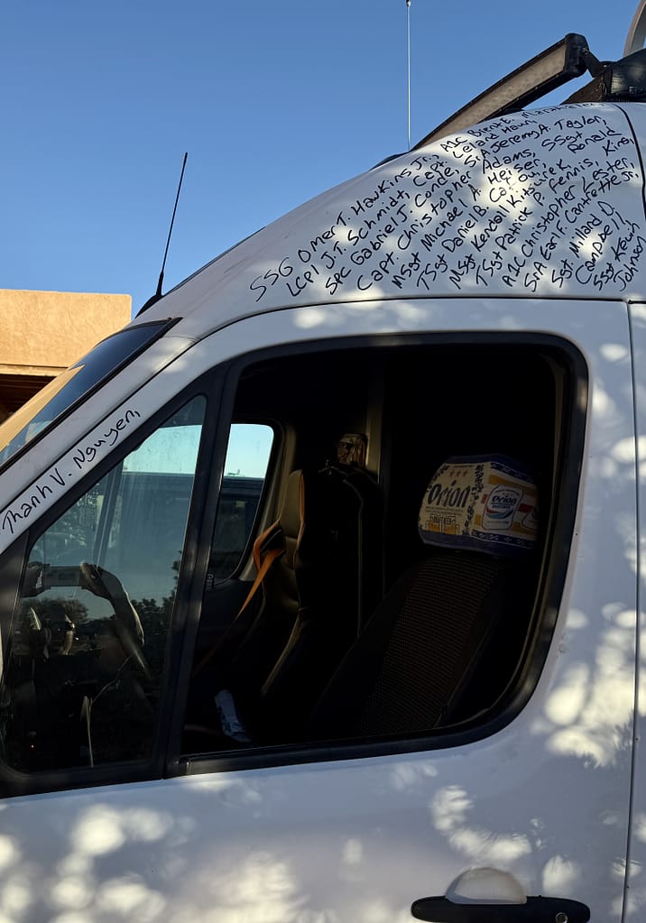 Close-up of a van door featuring handwritten names and military ranks on the roof, symbolizing honor and remembrance of fallen heroes.