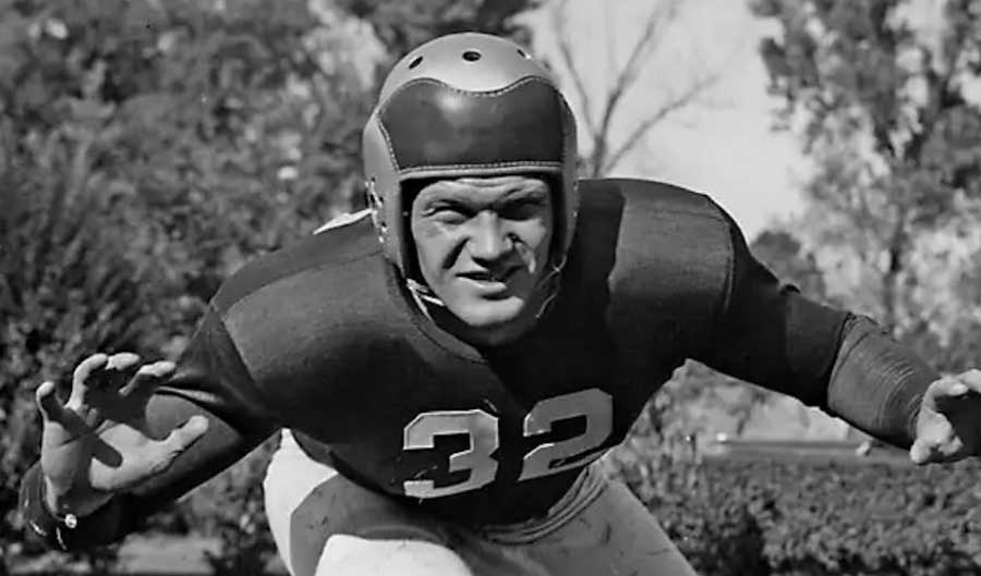 A vintage black and white photograph of a football player in a uniform with the number 32, wearing a helmet and posing in a dynamic, ready stance.